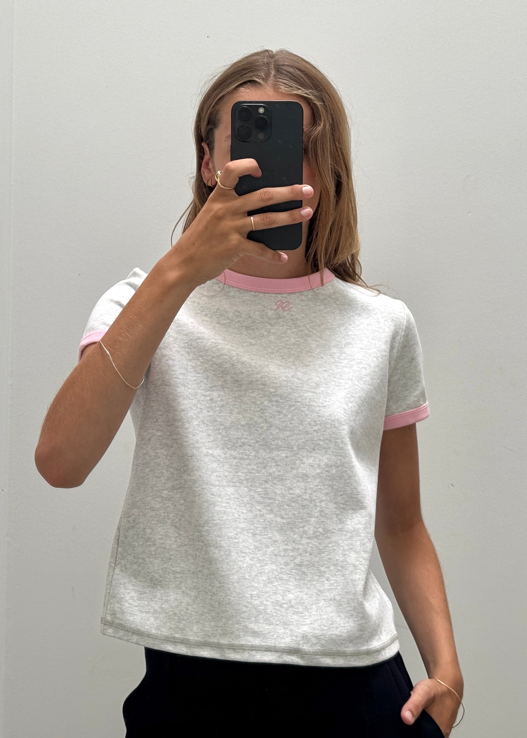 A person taking a mirror selfie wearing a light heather gray ringer t-shirt with pink trim on the collar and sleeve cuffs.