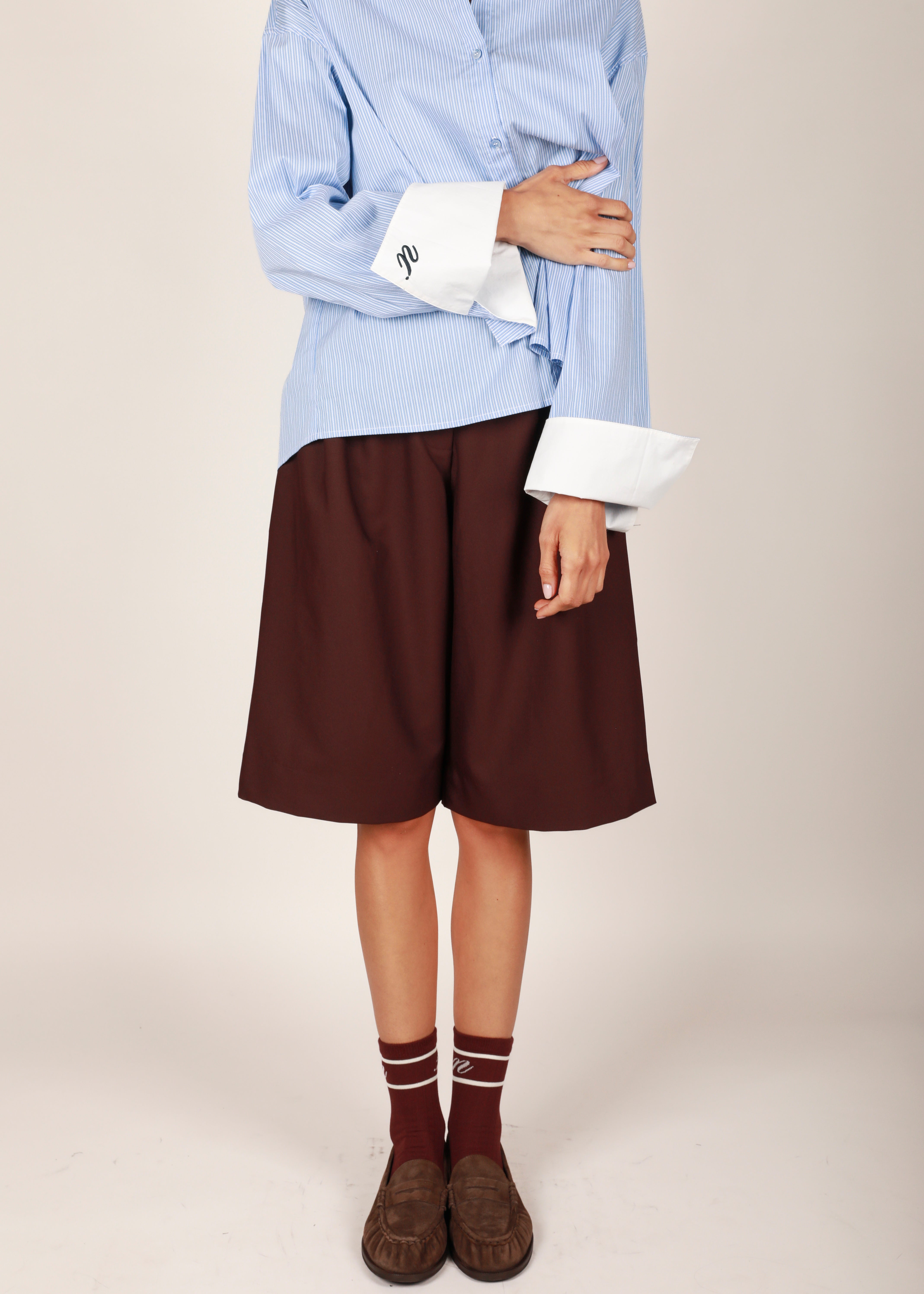 NOTED ANTWERP. A pair of high-waisted, wide-leg shorts in a deep reddish-brown or rust color, featuring pleated detailing at the front waist, laid flat against a light gray background.