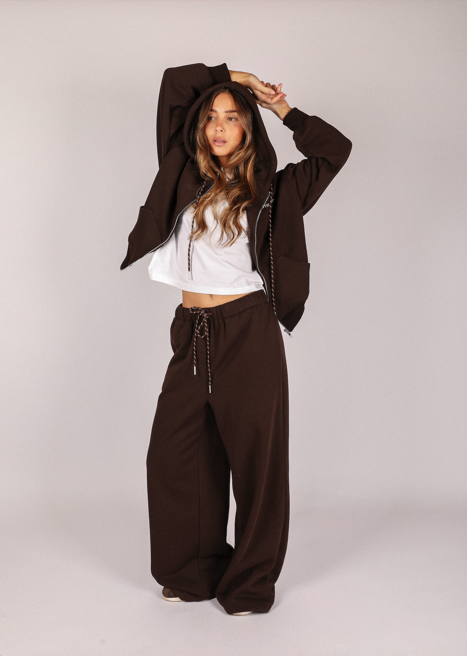 Person wearing a brown hoodie and wide-leg pants on a plain background