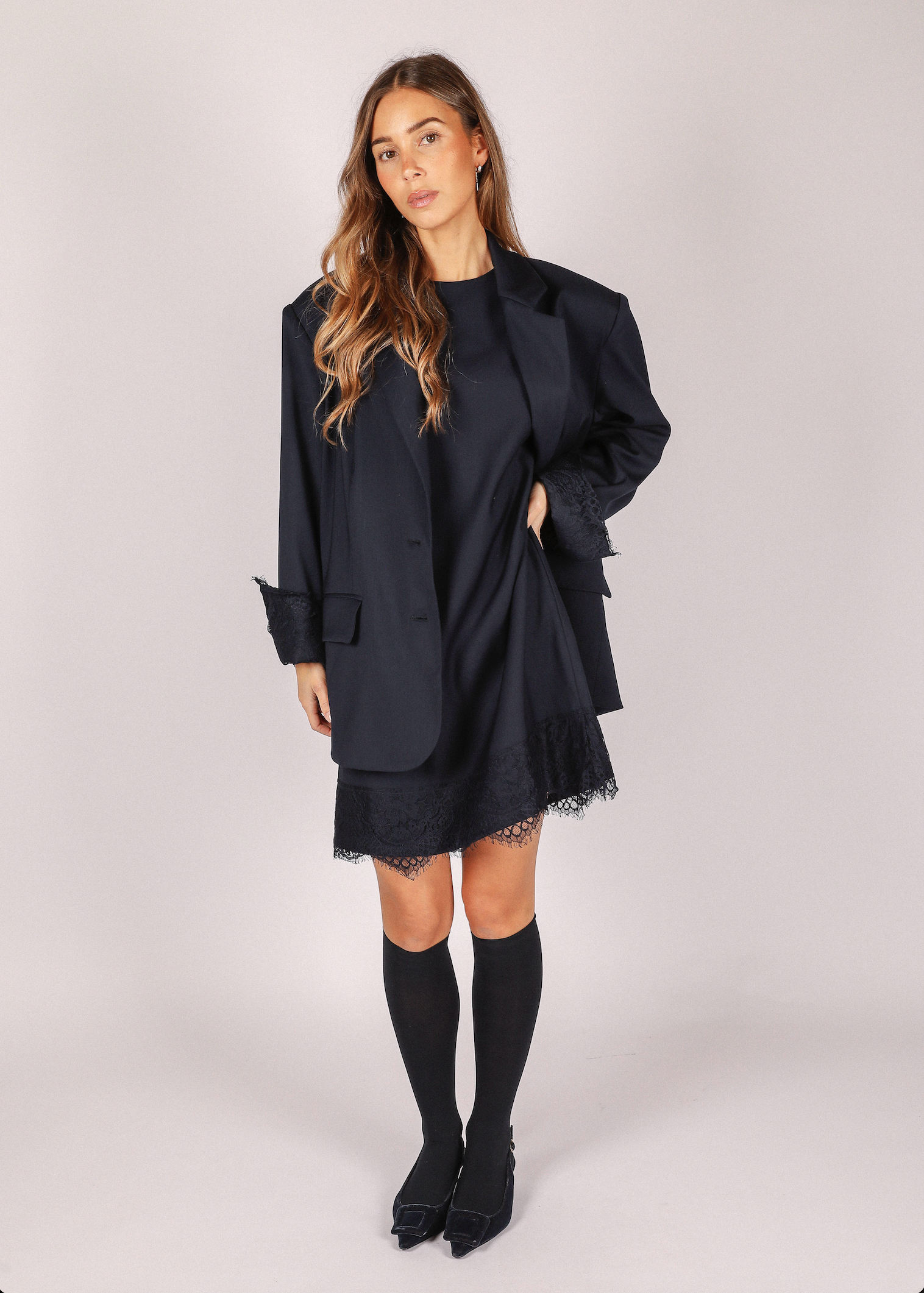 Woman wearing a navy arie blazer from noted antwerp over a dress on a plain background