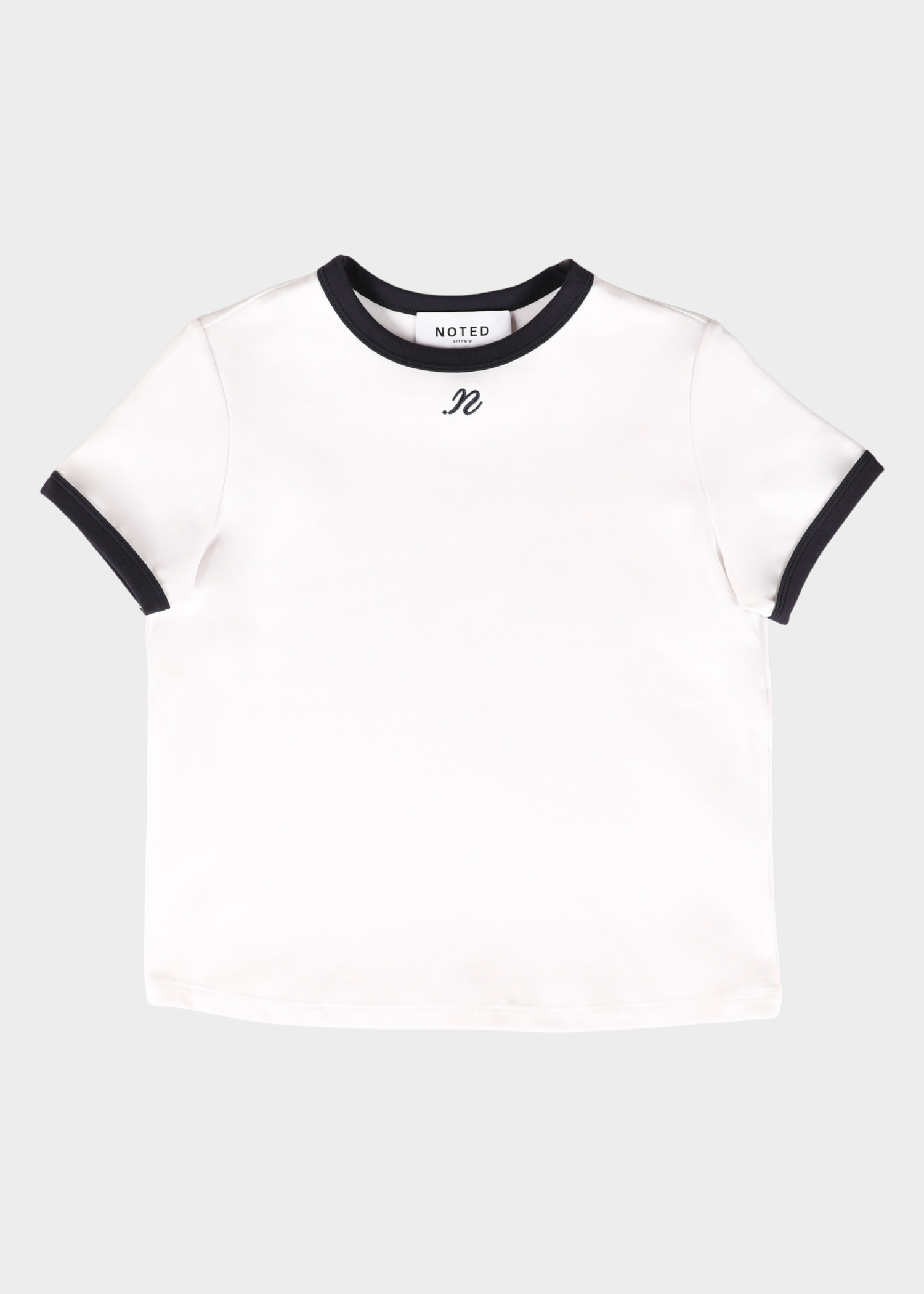A white ringer t-shirt with black trim on the crew neck and sleeve cuffs, featuring a small black embroidered monogram logo on the chest. The brand name 'NOTED' is visible inside the collar.