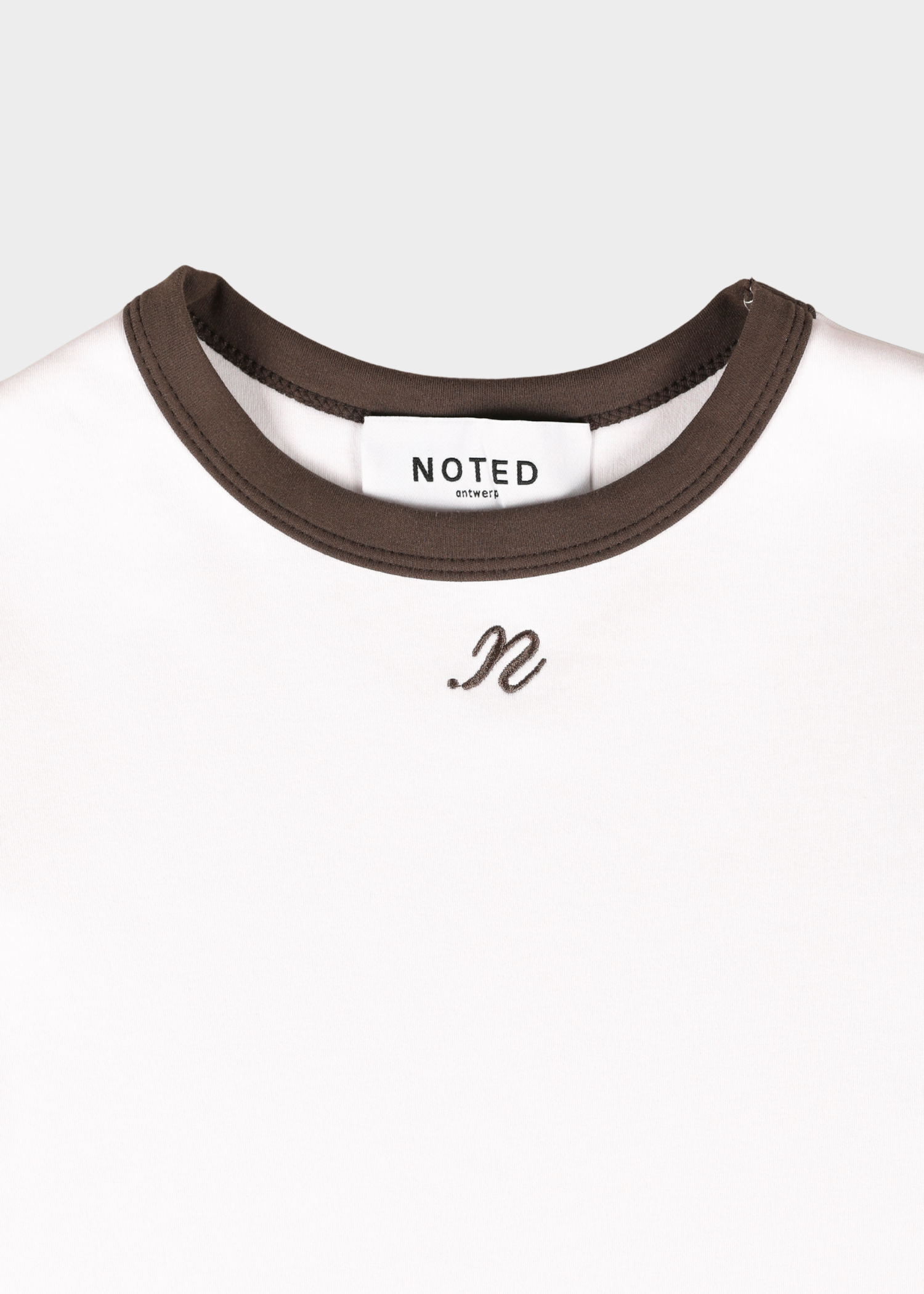 Close-up of a white T-shirt with a dark brown ribbed crew neck and a small black script logo on the chest. The inside neck label reads 'NOTED'