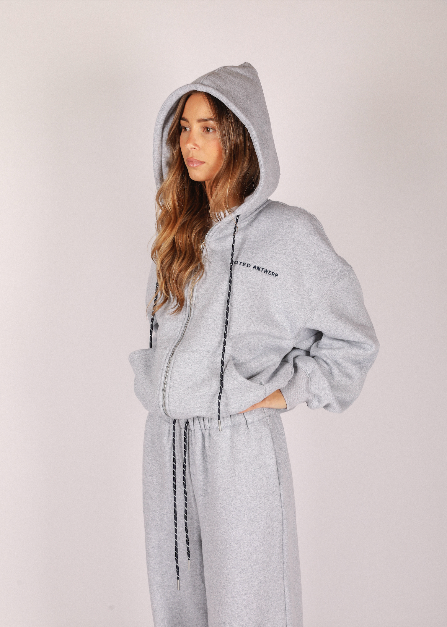 Woman wearing a gray hoodie and pants on a plain background